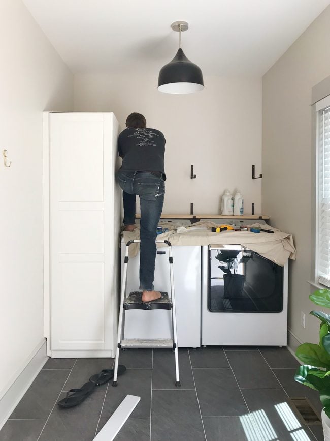 john leaning over top loading washer to screw in shelf brackets