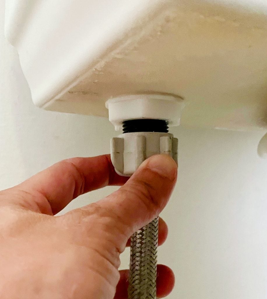 Hand Loosening Water Supply Line Under Toilet Tank