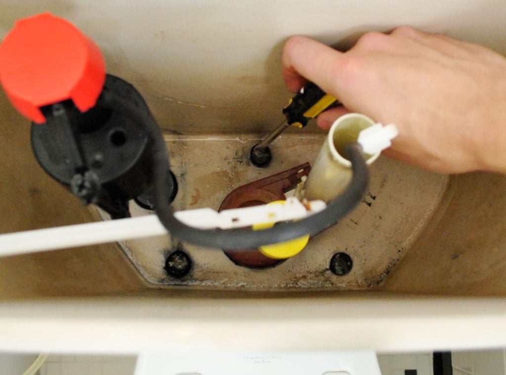 Hand Unscrewing Bolts Inside Toilet Tank