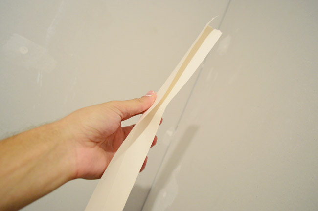 hand folding drywall tape along seam before pressing in corner