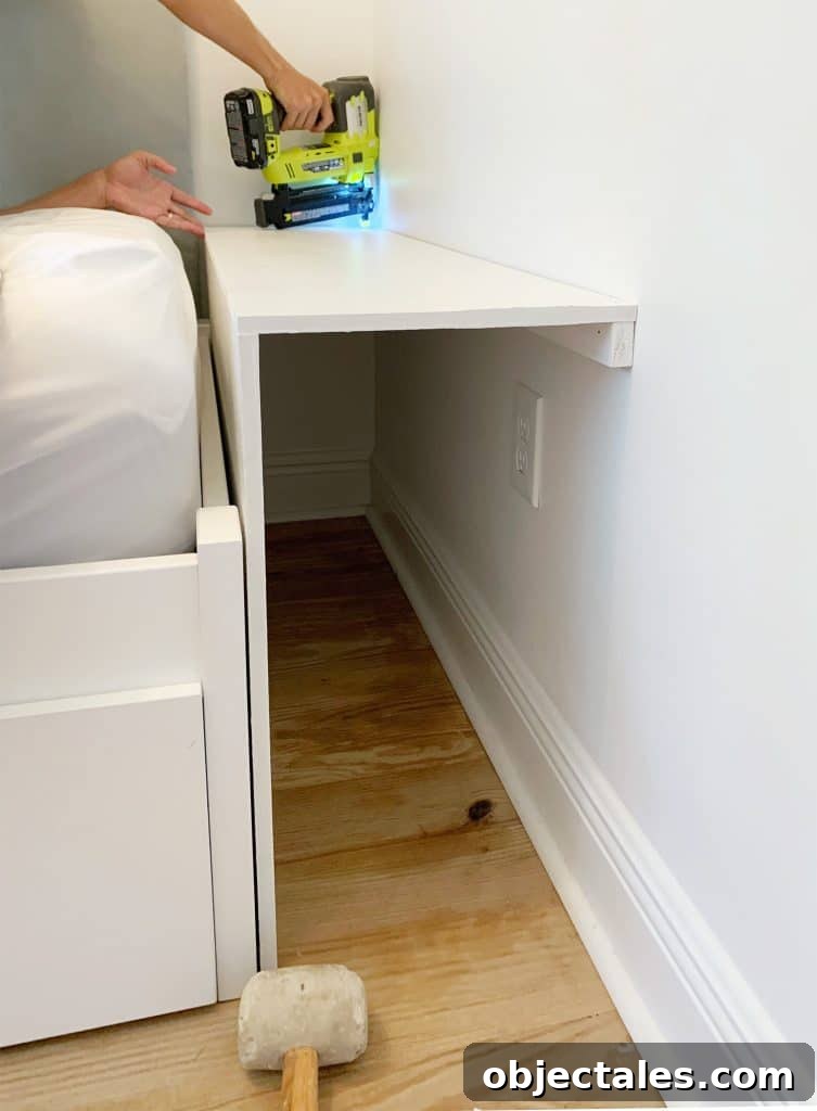 DIY Bookshelf: Step-by-Step Build Guide 6 Painted pieces of MDF being nailed in for bottom shelf of built-in bookcase