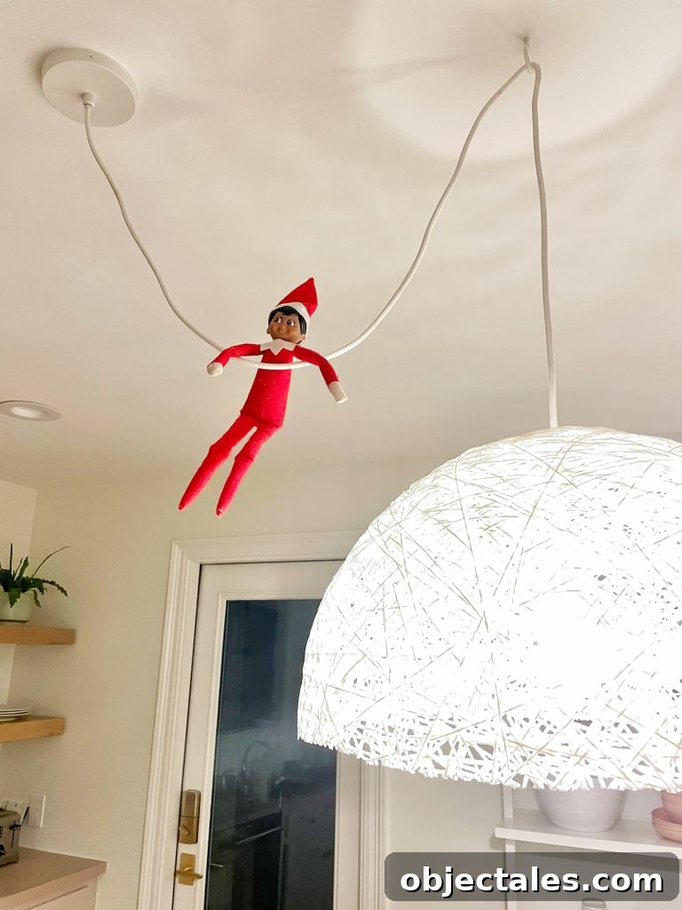 Elf on the Shelf hanging from pendant light cord in kitchen