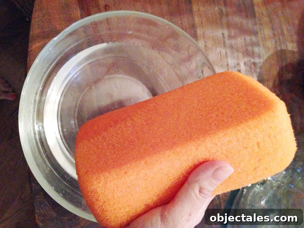 How to Remove Wallpaper Without Damaging Walls 14 Hand holding orange sponge over bowl