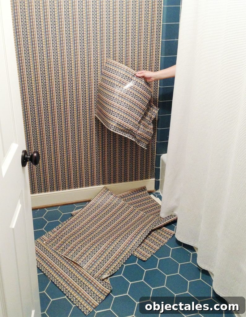 How to Remove Wallpaper Without Damaging Walls 9 Hand removing wallpaper from shower in blue bathroom