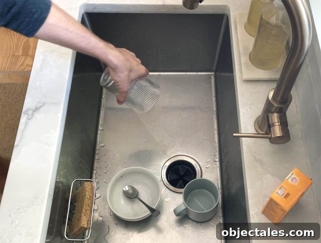 Hand removing dirty glass from dirty stainless steel sink for cleaning