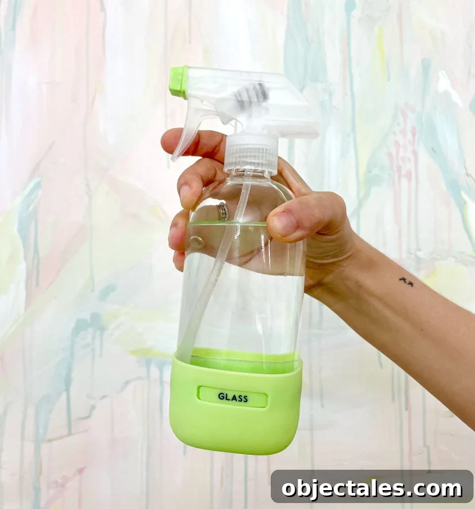 Hand Holding Homemade Window Cleaner In Glass Bottle In Front Of Colorful Painting