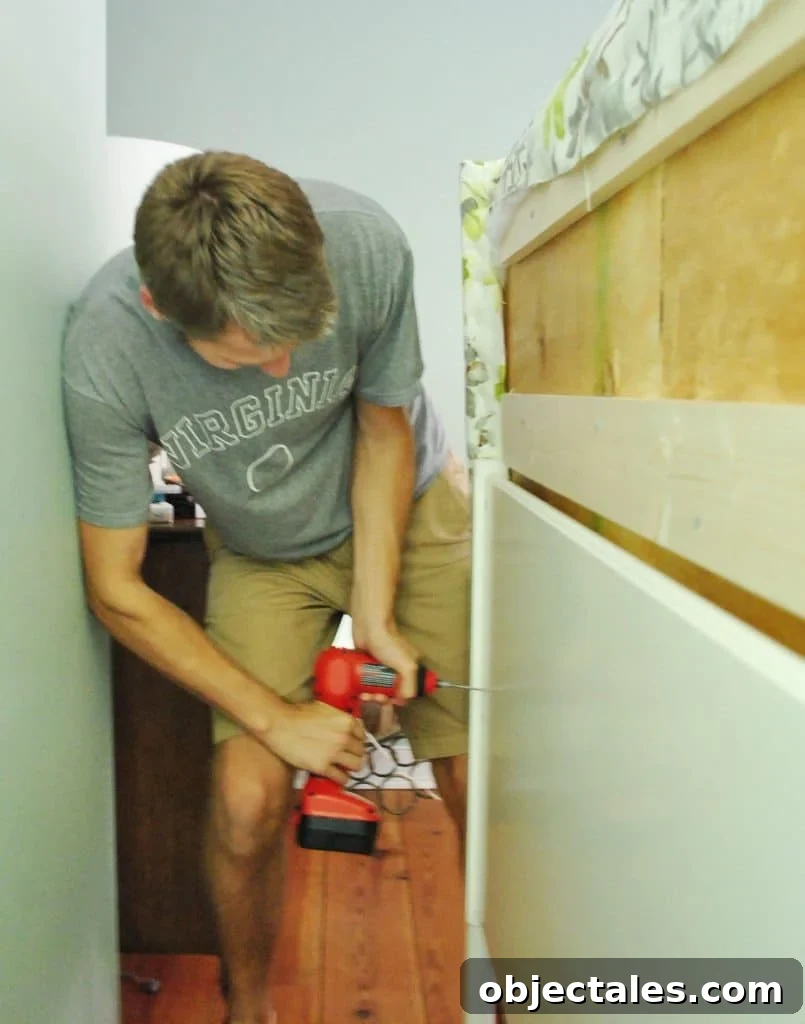John screwing DIY upholstered headboard onto frame from backside of bed