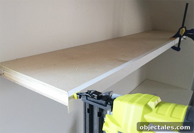 A Ryobi power nailer attaching face pieces of 1x2 pine wood board to thin white floating shelves in bonus room