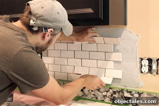 John placing white subway tile sheet onto mastic to set backsplash