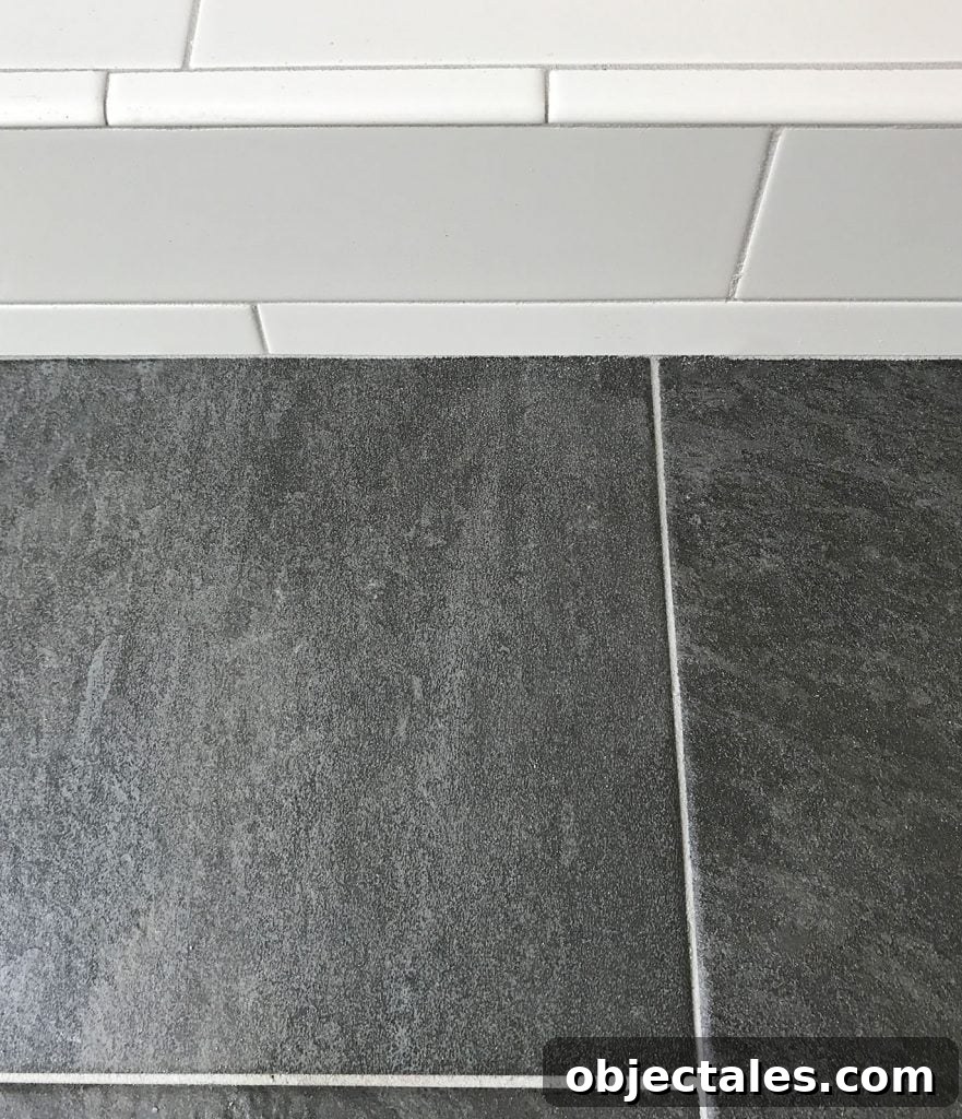 white subway tile shower next to dark slate floor with same gray grout