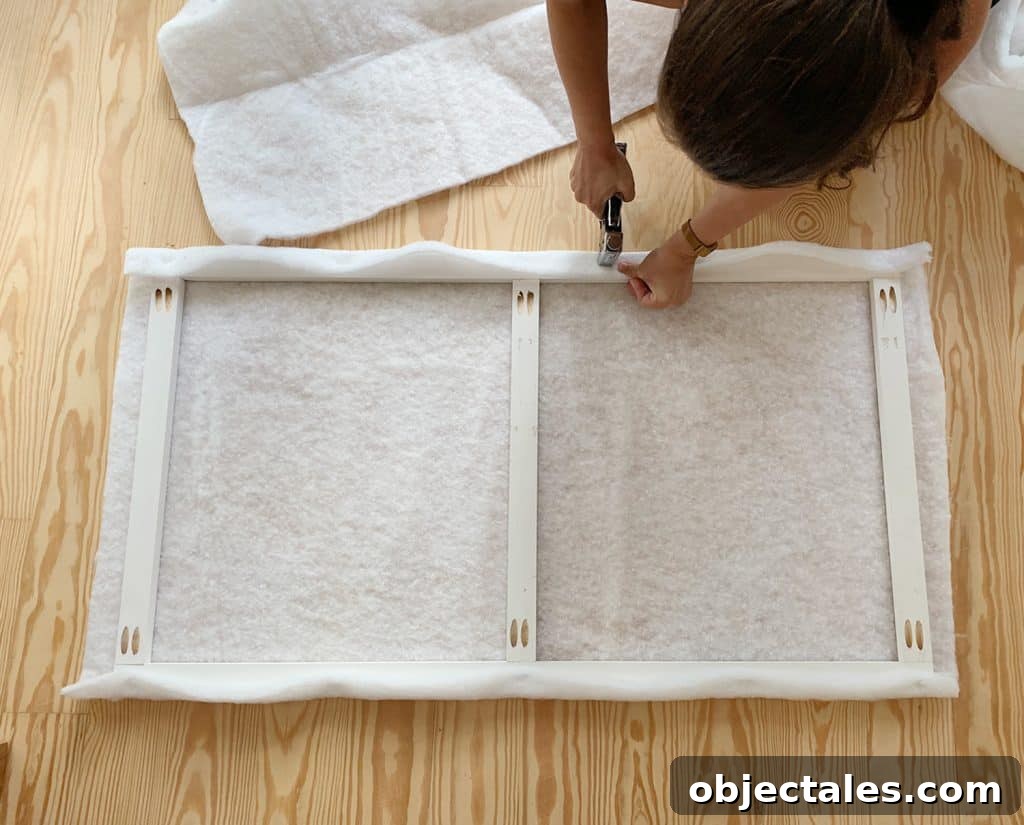 Build a Stylish DIY Headboard in One Weekend 7 Sherry stapling fabric batting around wood frame for DIY upholstered headboard