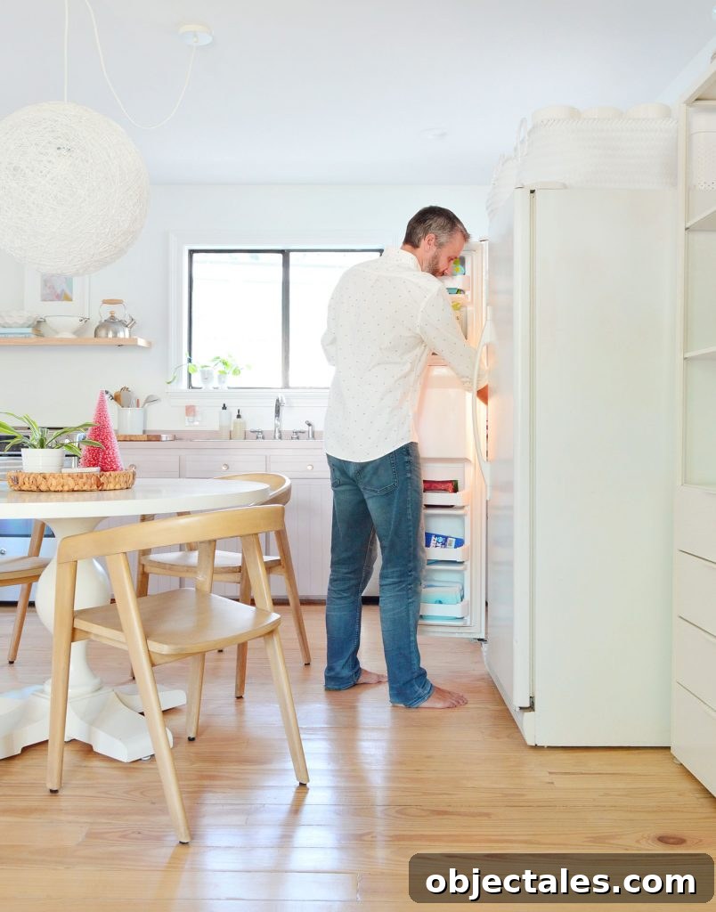 John standing with freezer door open next to round table in kitchen