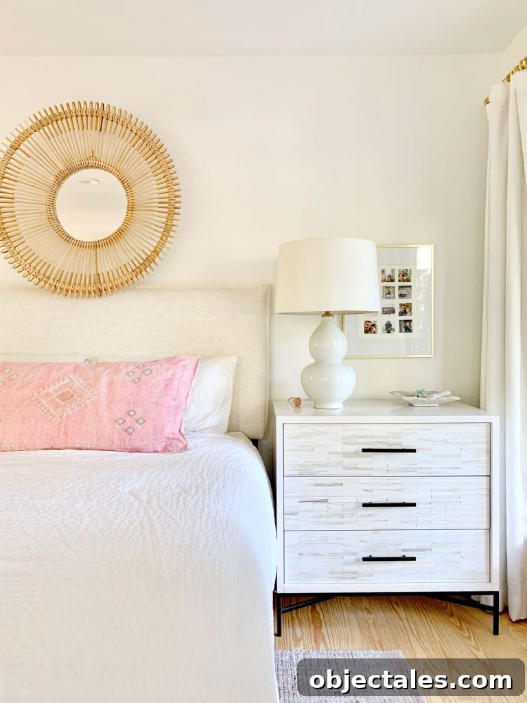 Linen headboard on bed with white bedding and inlay dresser as nightstand