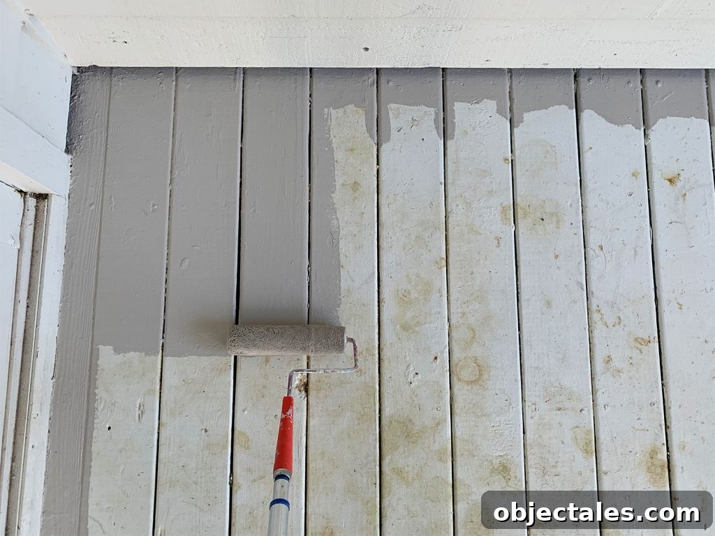 How to Paint a Porch Floor: Prep, Paint, and Finish 6 Roller applying gray porch paint to stained white porch floor